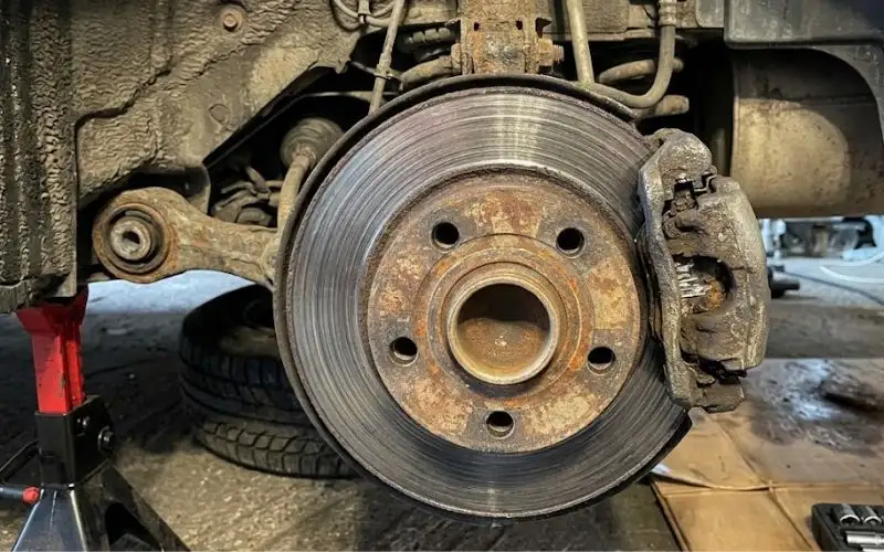Close-up view of a worn, rusty brake disc rotor and dragging caliper assembly during a vehicle brake inspection.